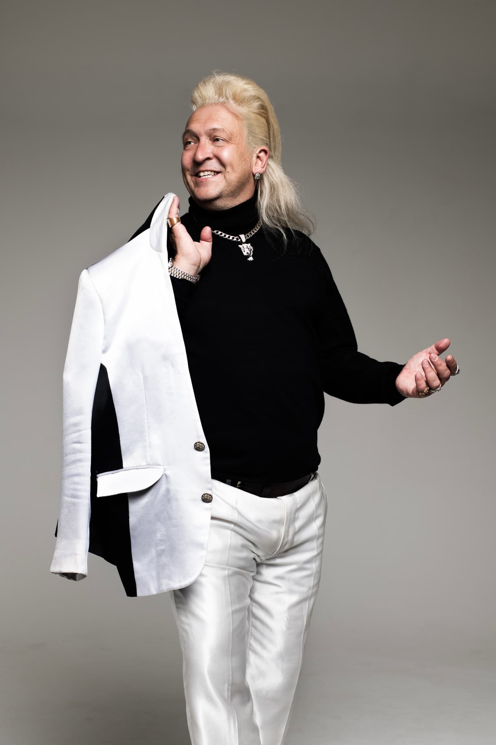 Clinton Baptiste, in a black jumper and white trousers, holding a white jacket over his shoulder