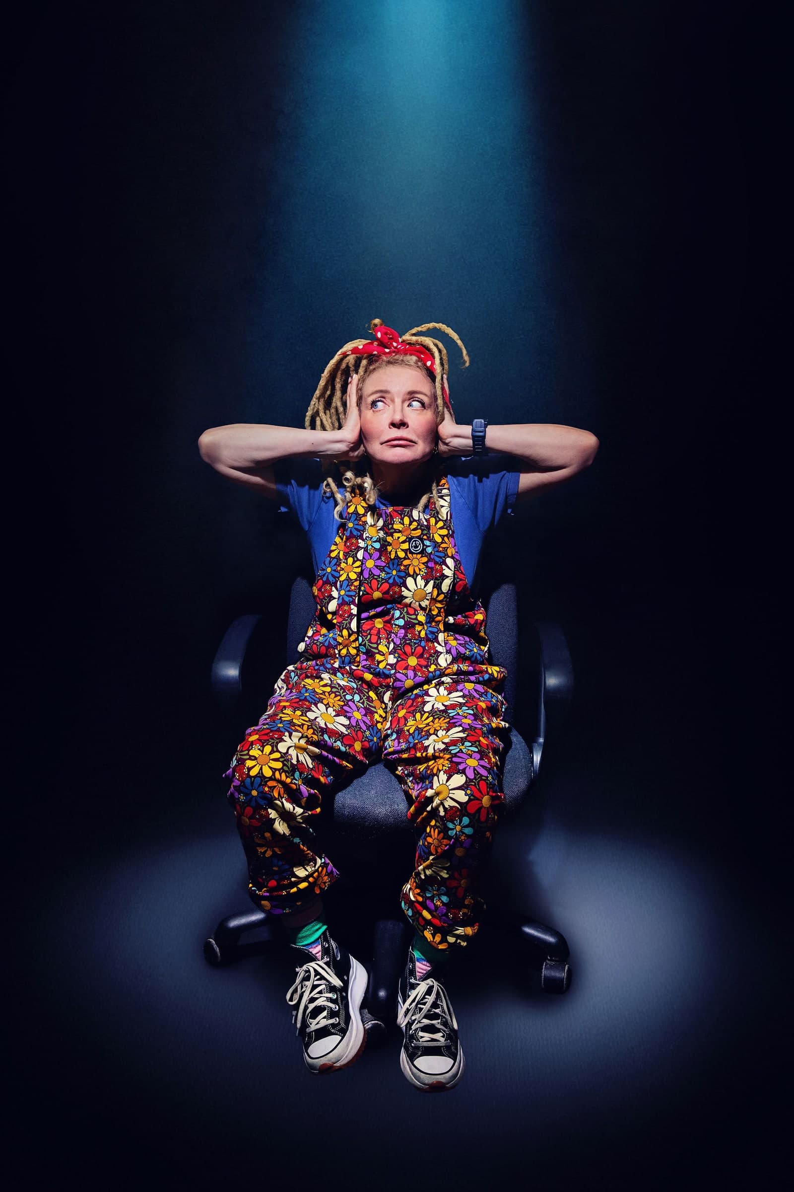 Samantha Day, comedian, sitting in a spotlight with her hands on her head