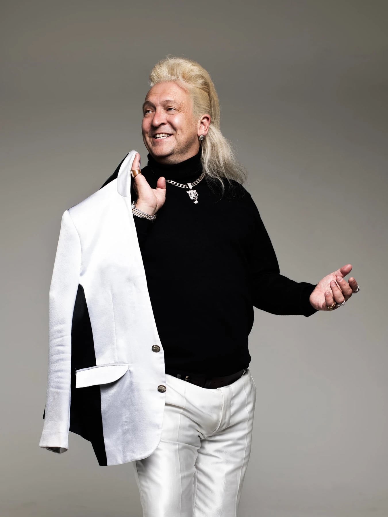 Clinton Baptiste, in a black jumper and white trousers, holding a white jacket over his shoulder