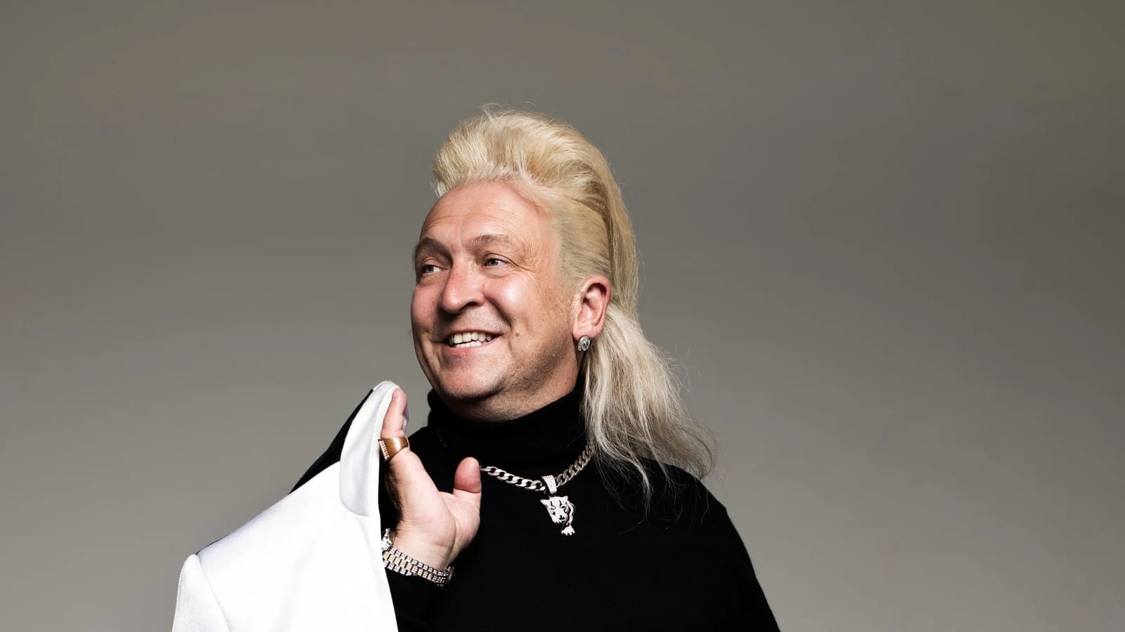 Clinton Baptiste, in a black jumper and white trousers, holding a white jacket over his shoulder